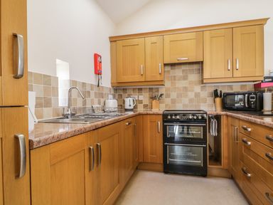 A kitchen with wooden cabinets a double oven a sink toaster kettle microwave and countertop at Skiddaw in Cockermouth