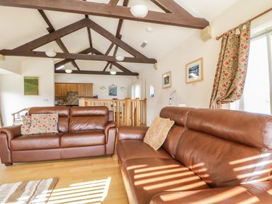 A living room with brown leather sofas wooden beams on the ceiling and a kitchen area at Skiddaw in Cockermouth