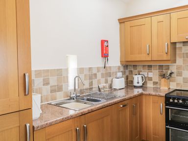 A kitchen with wooden cabinets a double sink a toaster kettle utensils and an oven at Skiddaw in Cockermouth