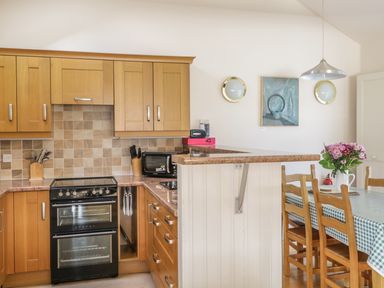 A kitchen with wooden cabinets and a black oven next to a dining table with a checkered tablecloth and flowers at Skiddaw in Cockermouth