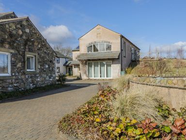 A paved driveway between two houses with a garden bed in the foreground at Skiddaw in Cockermouth