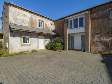 An exterior view of a two story building with a paved courtyard and multiple doors and windows at Esthers Barn in Cockermouth