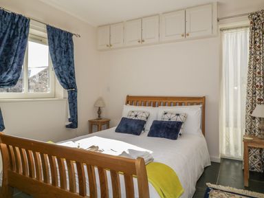 A bedroom with a wooden bed frame two bedside tables with lamps blue and patterned curtains and overhead storage cabinets at Esthers Barn in Cockermouth