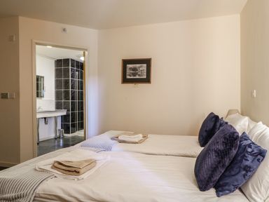 A bedroom with two single beds and an open door leading to a bathroom at Esthers Barn in Cockermouth