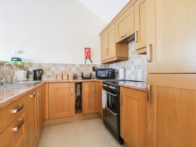 A kitchen with wooden cabinets a black stove a microwave kettle toaster and a sink at Esthers Barn in Cockermouth