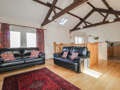 A living room with two black leather sofas and patterned cushions next to a red rug at Esthers Barn in Cockermouth