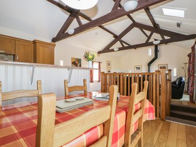 A dining area with a wooden table and chairs next to a kitchen counter in a room with exposed wooden beams and a railing at Esthers Barn in Cockermouth
