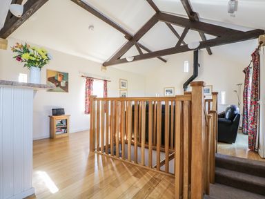 An open living area with wooden floor beams wooden stair railing black leather chairs and colorful curtains at Esthers Barn in Cockermouth