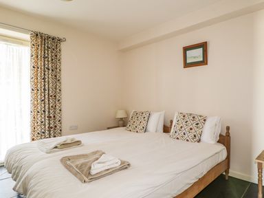 A bedroom with a double bed two patterned pillows towels on the bed a bedside table with a lamp and a window with patterned curtains at Beckside in Cockermouth