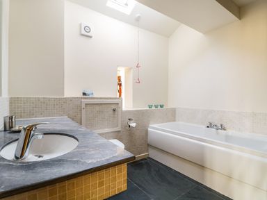 A bathroom with a sink on a dark countertop and a bathtub with tiled walls at Beckside in Cockermouth