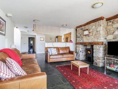 A living room with two brown leather sofas a red rug a wooden coffee table a stone fireplace with a wood stove and a television on a stand at Beckside in Cockermouth