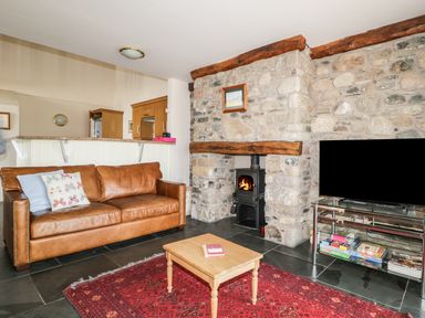 A living room with a brown leather sofa a wood stove in a stone fireplace and a flat screen tv on a stand at Beckside in Cockermouth