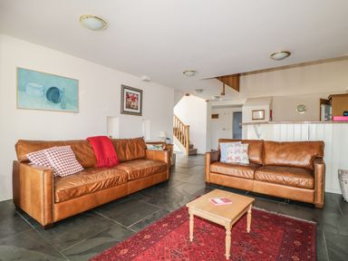 A living room with two brown leather sofas a small wooden coffee table a red rug and framed pictures on the wall at Beckside in Cockermouth