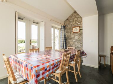 A dining room with a checkered tablecloth on a table surrounded by wooden chairs and glass doors at Beckside in Cockermouth