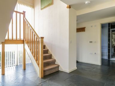 A staircase with wooden railing and carpeted steps in a hallway with tiled floor and a doorway leading to a bathroom at Beckside in Cockermouth