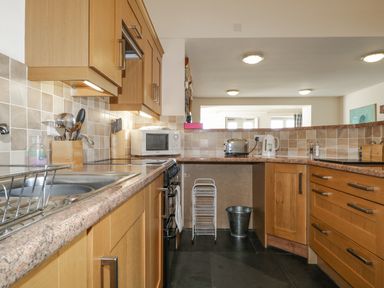 A kitchen with wooden cabinets a microwave toaster kettle and utensils at Beckside in Cockermouth