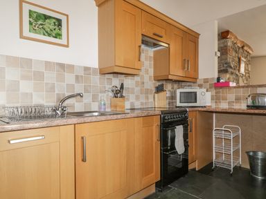 A kitchen with wooden cabinets a black stove microwave sink and utensil holders at Beckside in Cockermouth