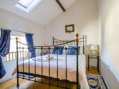 A bedroom with a metal bed frame with white bedding and blue pillows a lamp on a glass side table and blue curtains at Beckside in Cockermouth