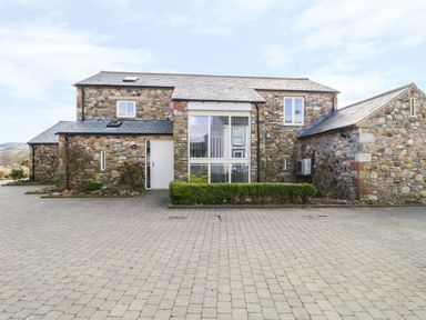 A stone house with a paved driveway and green bushes at Beckside in Cockermouth