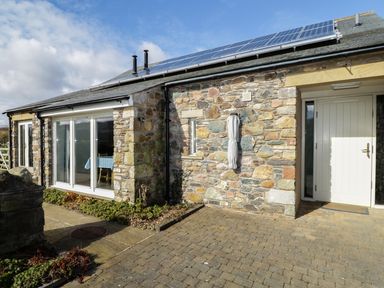 The exterior of a stone house with solar panels on the roof a white door and sliding glass doors at Buttermere in Cockermouth