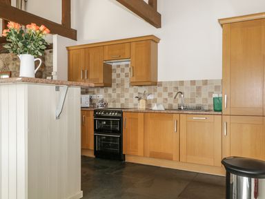 A kitchen with wooden cabinets a stove a sink a trash bin and flowers on a counter at Buttermere in Cockermouth