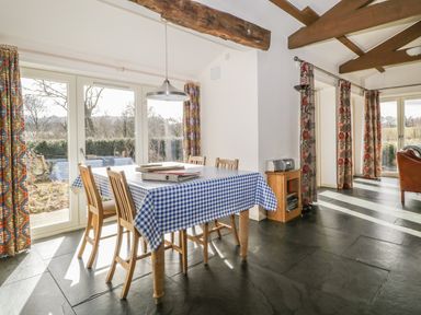 A dining area with a wooden table covered by a blue and white checkered tablecloth and wooden chairs near large glass doors with patterned curtains at Buttermere in Cockermouth