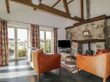 A living room with leather sofas a stone fireplace a flat screen tv and large windows with floral curtains at Buttermere in Cockermouth