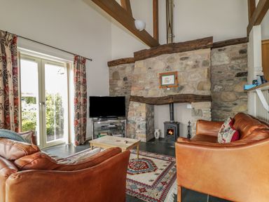 A living room with two leather sofas a wooden coffee table a television a stone fireplace and a patterned rug at Buttermere in Cockermouth