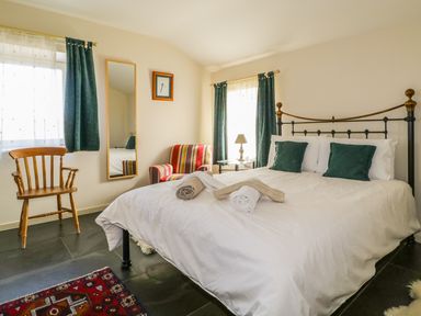 A bedroom with a bed with green pillows two rolled towels armchair wooden chair mirror and windows with curtains at Buttermere in Cockermouth