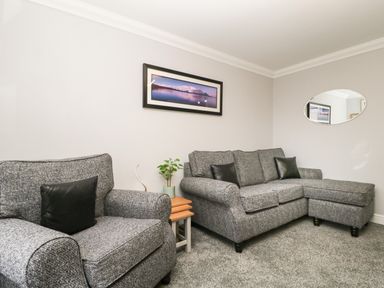 A living room with two grey sofas, a small wooden side table with a plant, a landscape picture on the wall, and an oval mirror at Andra Ghyll in Keswick