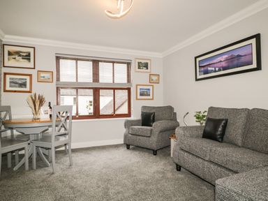 A living room with grey sofa and armchair a wooden table and chairs and framed pictures on the walls at Andra Ghyll in Keswick