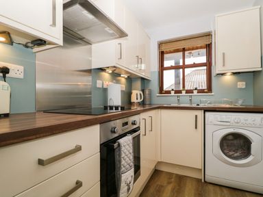 A kitchen with white cabinets and brown countertops including a stove oven washing machine and window at Andra Ghyll in Keswick