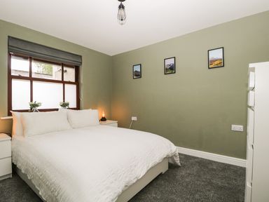 A bedroom with a white bed and bedside tables under a window with a grey blind at Andra Ghyll in Keswick