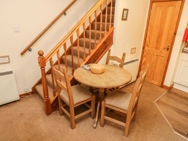 A small dining area with a round wooden table and three chairs next to a carpeted staircase at Juniper Cottage in Ambleside