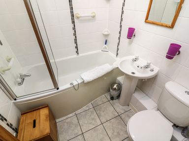 A bathroom with a bathtub shower sink toilet mirror and wooden cabinet at Juniper Cottage in Ambleside
