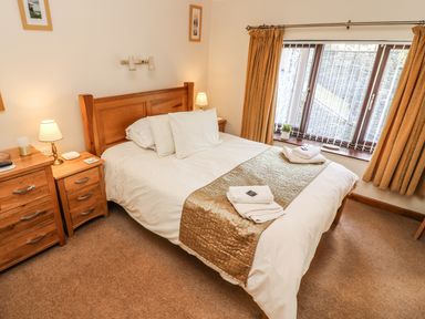 A bedroom with a double bed linens bedside tables with lamps and a window with curtains at Juniper Cottage Ambleside