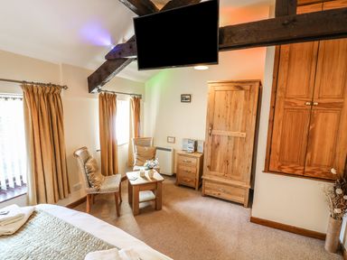 A bedroom with two chairs and a small table between wooden wardrobes and a hanging television at Juniper Cottage in Ambleside