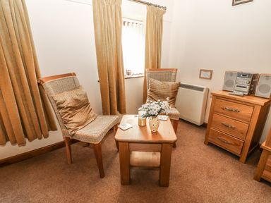 A sitting area with two wicker chairs with cushions a wooden table with flowers and a small wooden chest with a stereo at Juniper Cottage in Ambleside