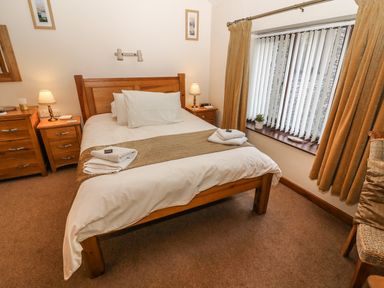 A bedroom with a wooden double bed white bedding two bedside tables with lamps window with vertical blinds and brown curtains at Juniper Cottage in Ambleside