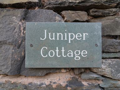 A stone plaque with the text Juniper Cottage mounted on a stone wall at Juniper Cottage Ambleside