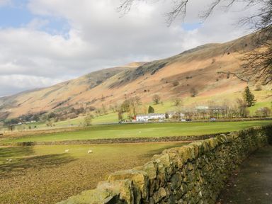 A rural landscape with stone walls trees and sheep in a field with hills in the background at The Hayloft in Thirlmere