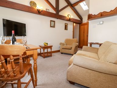 A sitting room with a sofa armchair wooden dining table and television at The Hayloft in Thirlmere