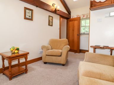 A sitting area with beige armchairs wooden side tables and framed pictures on the wall at The Hayloft in Thirlmere