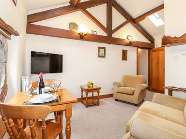 A living room with wooden beams a dining table set with plates and wine and armchairs at The Hayloft in Thirlmere