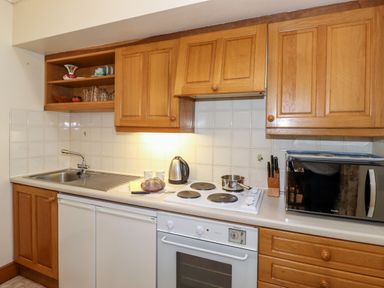 A kitchen with wooden cabinets a sink an electric stove an oven a microwave kettle and a loaf of bread at The Hayloft in Thirlmere