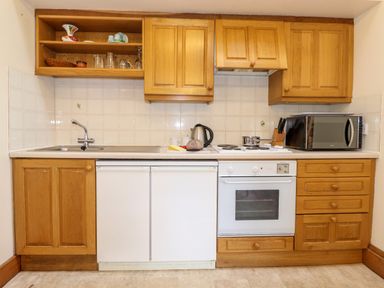 A kitchen with wooden cabinets a sink an oven a microwave and a kettle on the counter at The Hayloft in Thirlmere