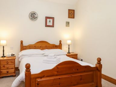 A bedroom with a wooden bed and bedside tables with lamps and folded towels on the bed at The Hayloft in Thirlmere