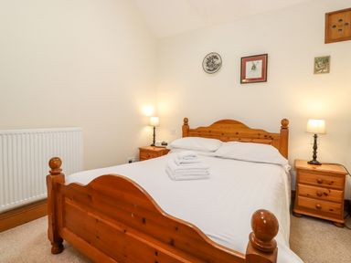A bedroom with a wooden bed and bedside tables with lamps at The Hayloft in Thirlmere