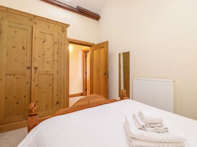 A bedroom with a wooden bed, wardrobe, wall mirror, radiator, and folded towels on the bed at The Hayloft in Thirlmere