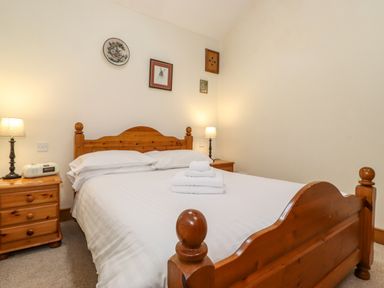 A bedroom with a wooden double bed white bedding bedside tables with lamps and folded towels on the bed at The Hayloft in Thirlmere